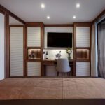 Modern bedroom with a desk, chair, and TV mounted on the wall.