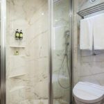 Modern bathroom with glass shower enclosure and marble walls.