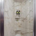 Modern shower with marble walls and built-in shelves holding shampoo bottles.
