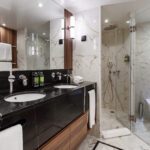 Modern bathroom with marble shower and black countertop vanity.