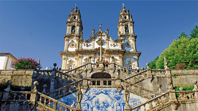 Baroque church with twin towers and ornate staircase under clear blue sky.