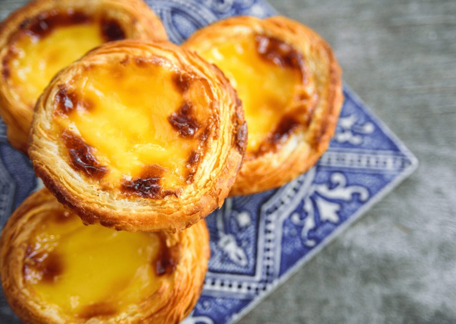 Golden Portuguese egg tarts on a blue patterned plate.