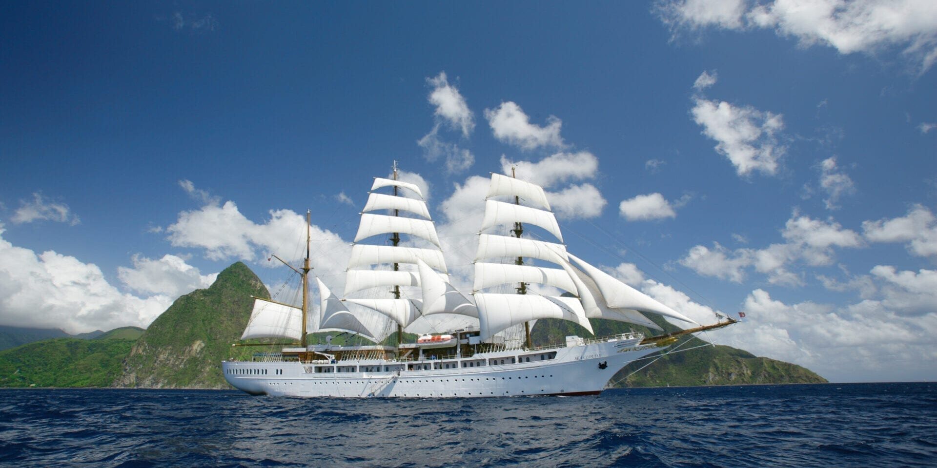 A majestic white sailing ship with multiple sails on the ocean under a blue sky.